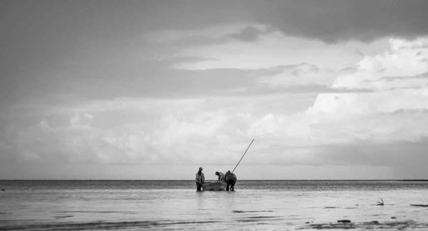 a couple of people that are standing in the water, a black and white photo, unsplash, minimalism, fishing boat, masai, on the sea, fineartamerica