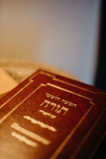 a book sitting on top of a bed next to a lamp, hebrew, red and gold cloth, a close up shot, square