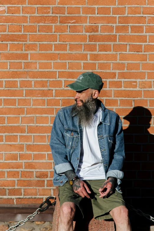 a man sitting on a bench next to a fire hydrant, an album cover, by Andrew Stevovich, pexels contest winner, long grey beard, denim jacket, green hat, profile image