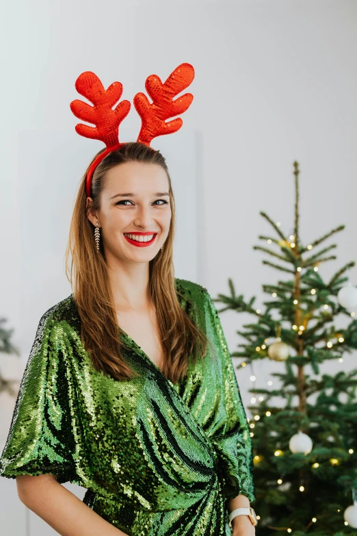 a woman standing in front of a christmas tree, a portrait, pexels, happening, antlers on her head, green robe, official product photo, smiling young woman