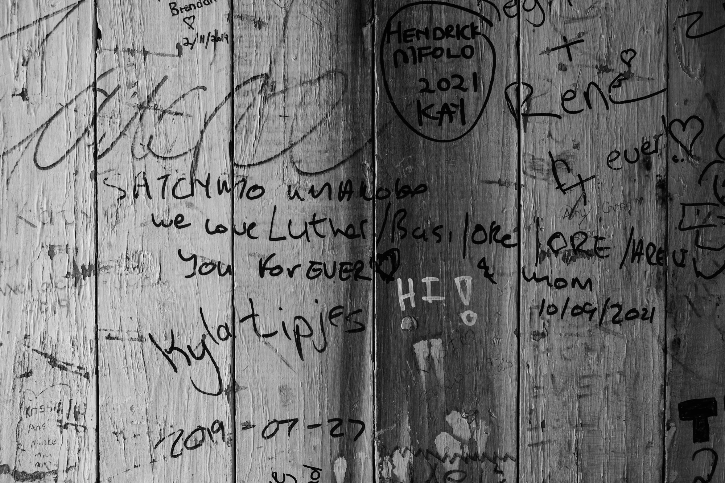 a black and white photo of graffiti on a wooden wall, an album cover, by Micha Klein, pexels, signatures, wooden toilets, messages, found on a volcano