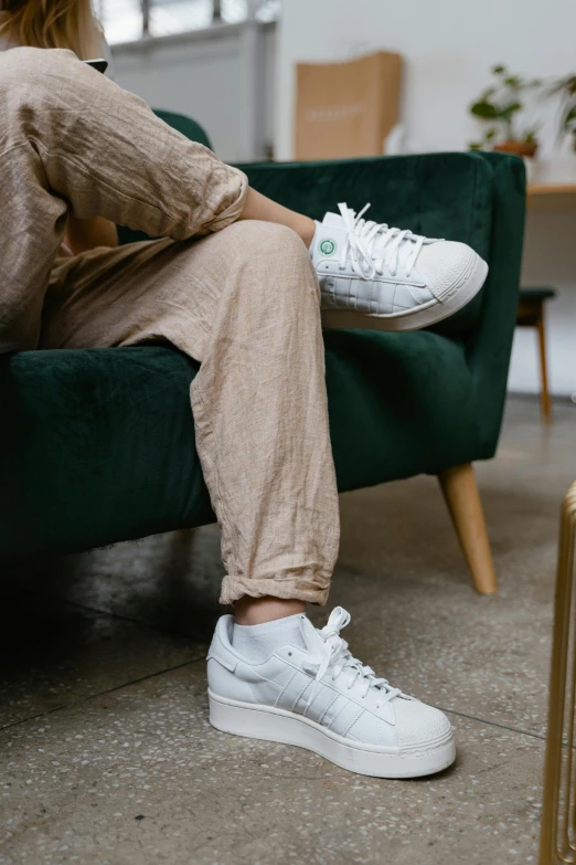 a woman sitting on top of a green couch, by Carlo Martini, trending on unsplash, white adidas pants, sustainable materials, sneaker, flax