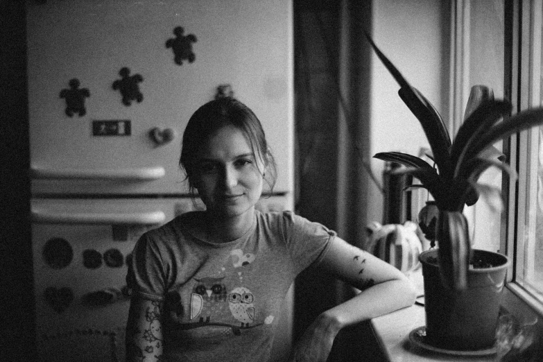 a woman sitting in front of a window next to a potted plant, a black and white photo, flickr, in the kitchen, early 2 0 0 0 s, with tattoos, aurora aksnes