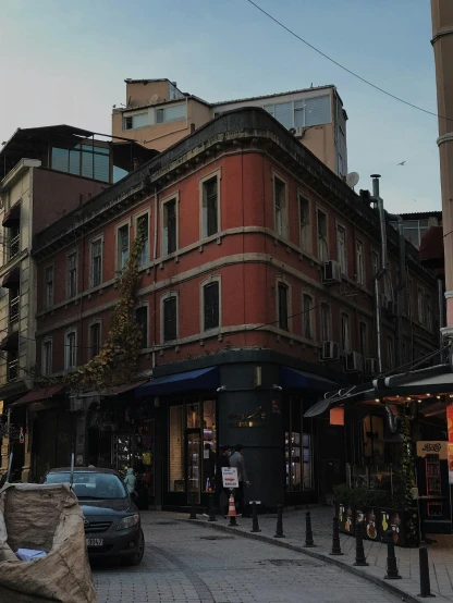 a car driving down a street next to tall buildings, a photo, pexels contest winner, art nouveau, location of a dark old house, ayanamikodon and irakli nadar, square, lots of shops