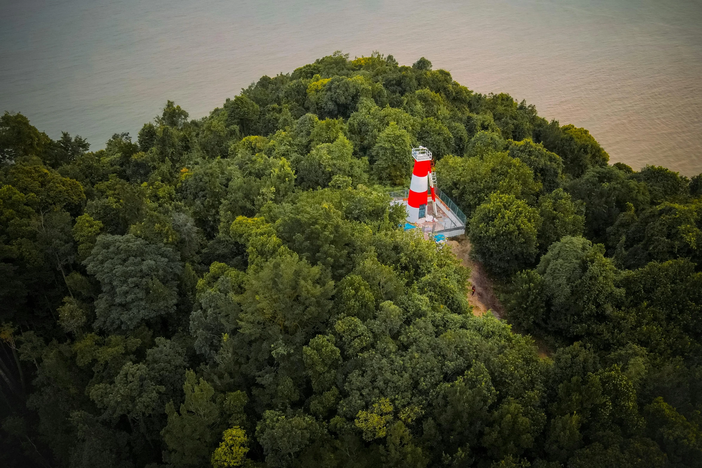 an aerial view of a lighthouse surrounded by trees, by Eglon van der Neer, unsplash contest winner, land art, slightly red, moomin, family friendly, slight haze