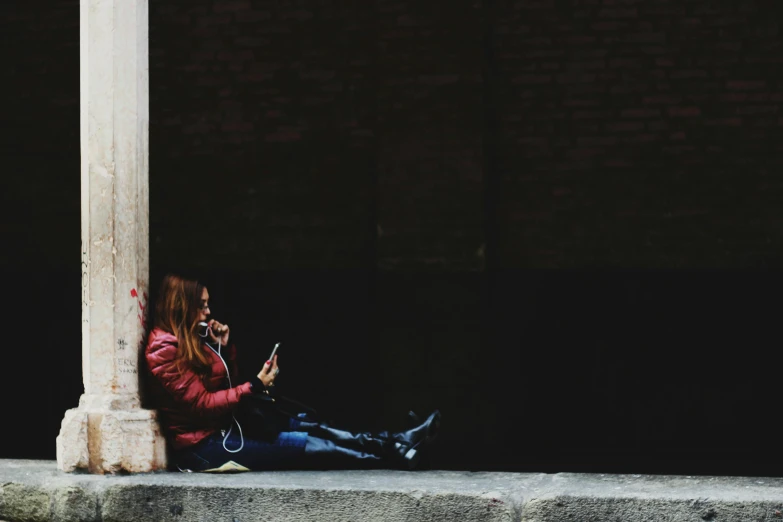 a woman sitting on a ledge using a cell phone, pexels contest winner, red wall, dark and grungy, with head phones, people on the ground