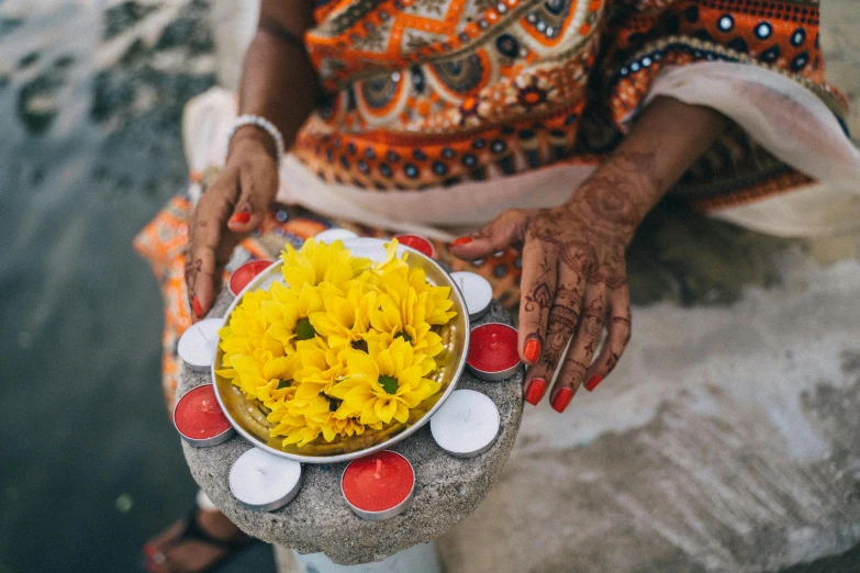 a woman holding a bowl of yellow flowers, pexels contest winner, hindu ornaments, candles, her hands are red roots, al fresco