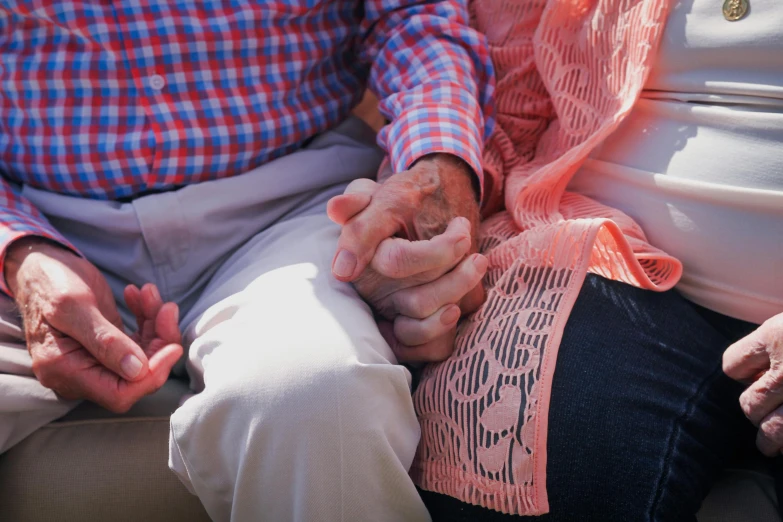 a close up of two people holding hands, coloured photo, older male, tight wrinkled cloath, sitting down