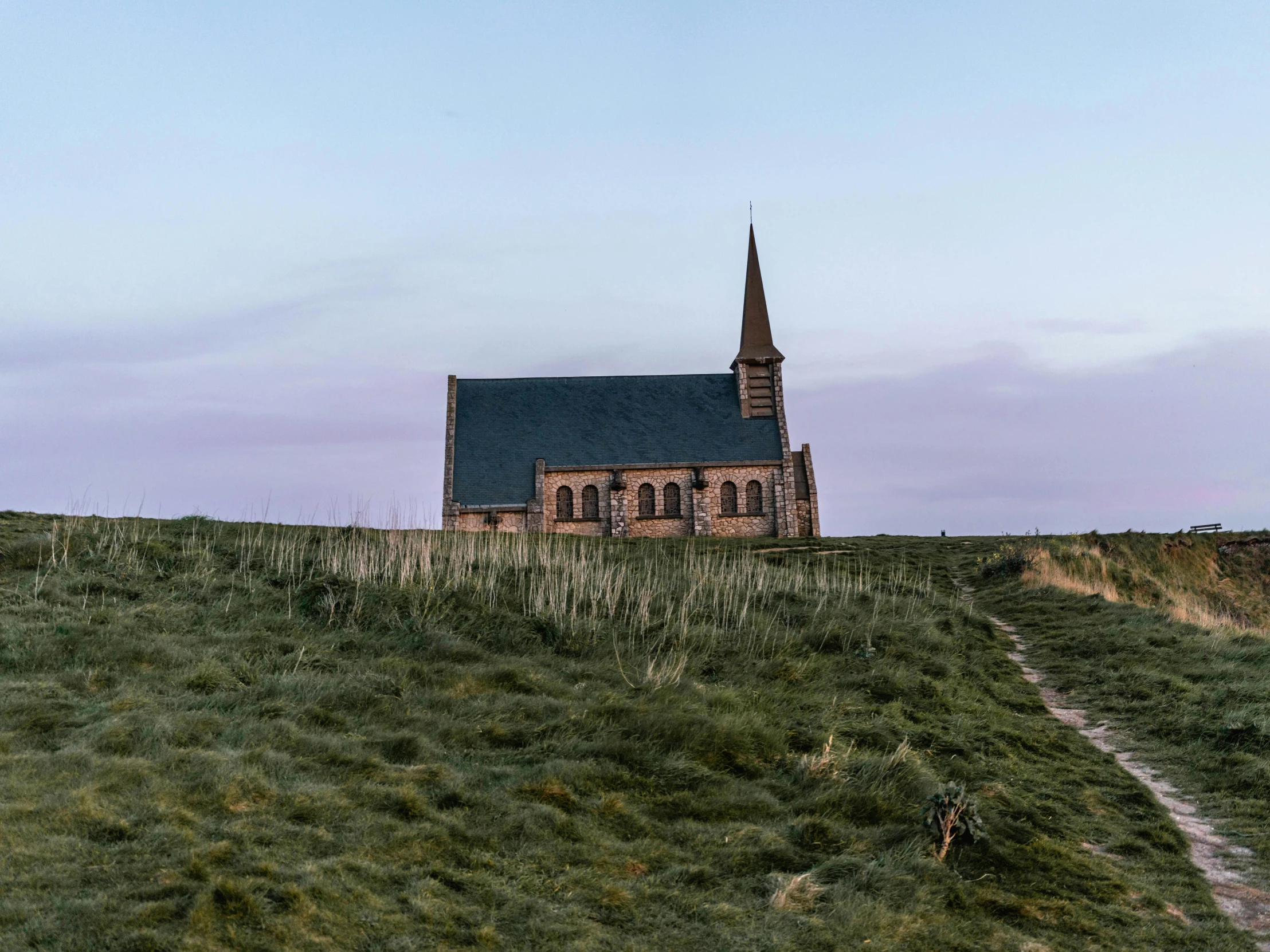 a church sitting on top of a lush green hillside, an album cover, by Jan Tengnagel, pexels contest winner, salt dunes, early evening, pale pink grass, northern france
