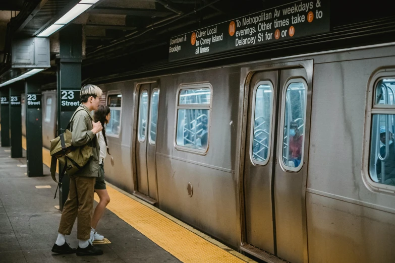a couple of people standing next to a train, by Carey Morris, pexels contest winner, mta subway entrance, thumbnail, watching new york, flattened