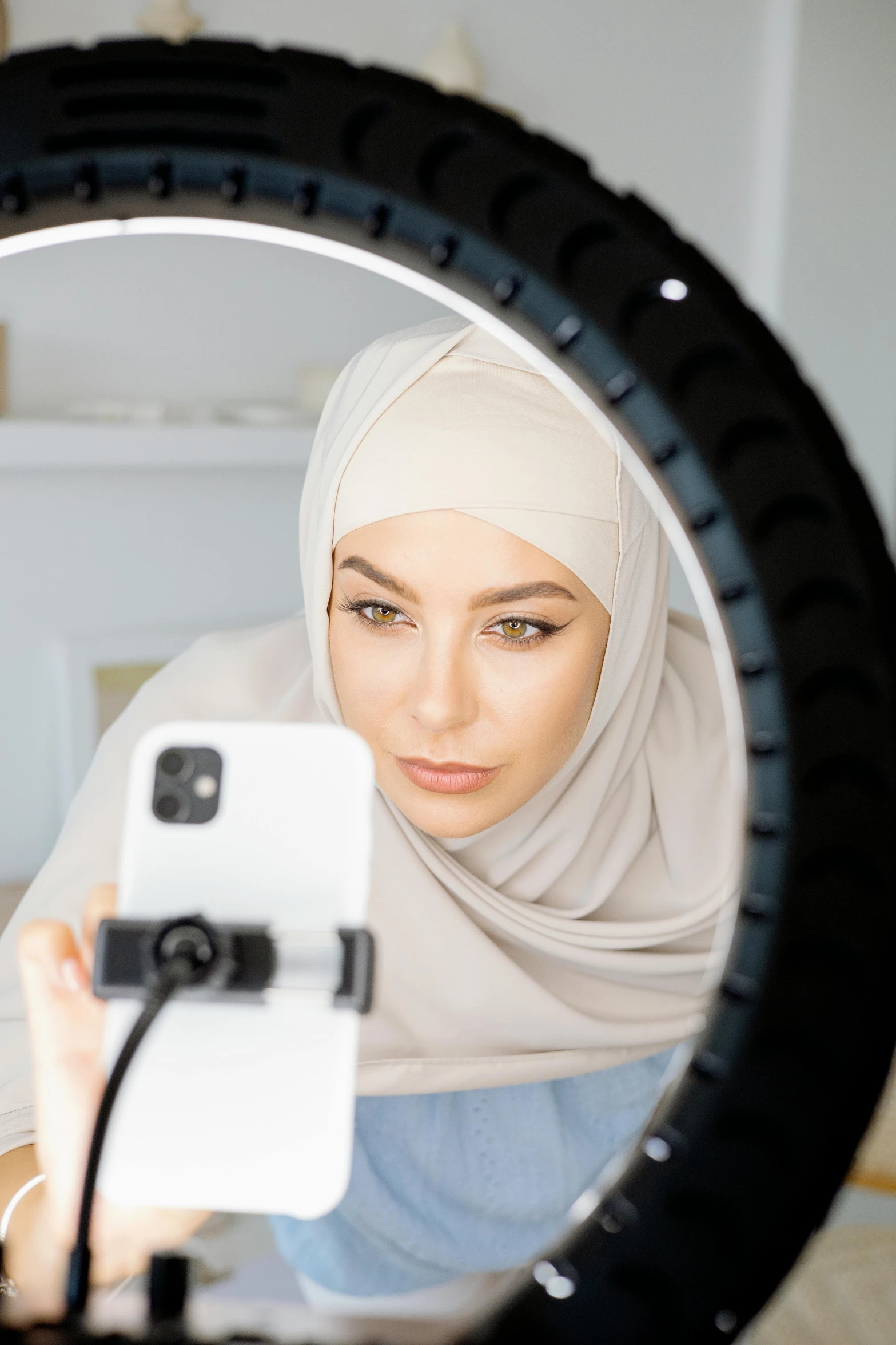 a woman taking a picture of herself in a mirror, hurufiyya, ring light, modest, official product photo, face centred