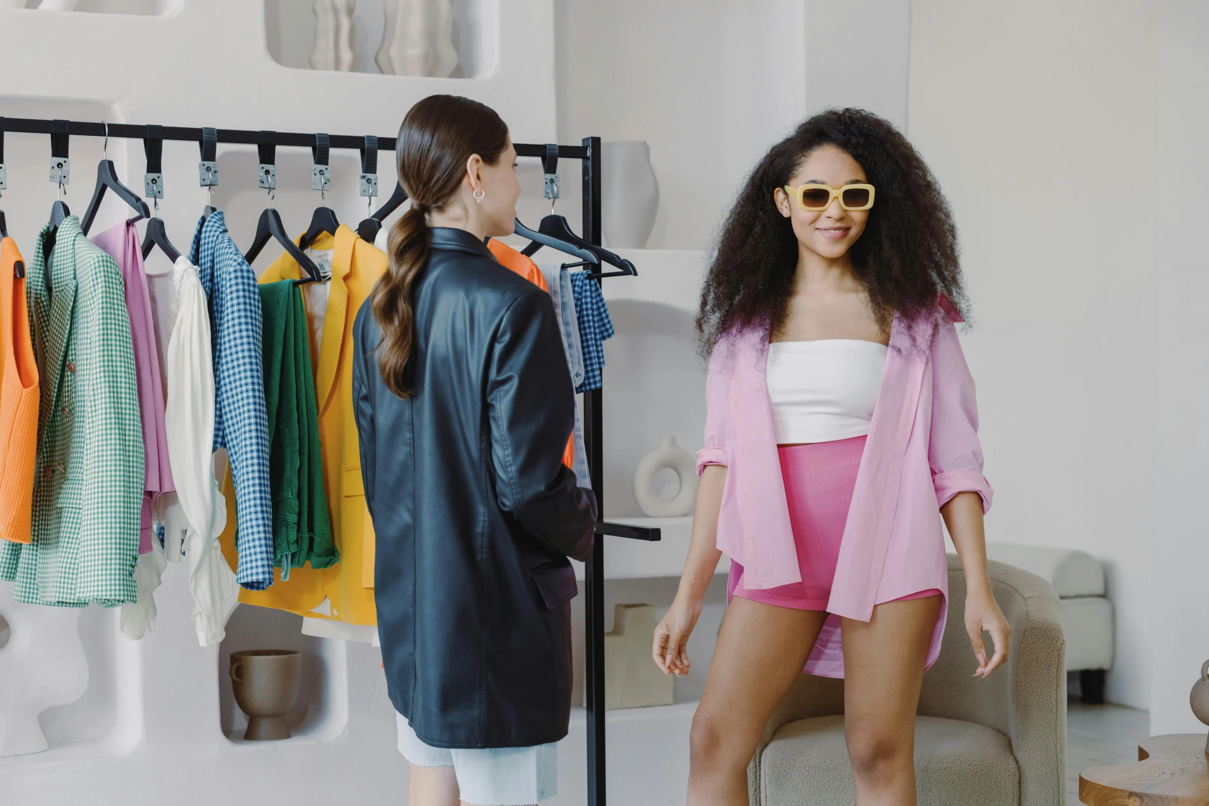 two women standing in front of a rack of clothes, trending on pexels, happening, pink and yellow, short skirt and a long jacket, wearing shades, photoshoot for skincare brand