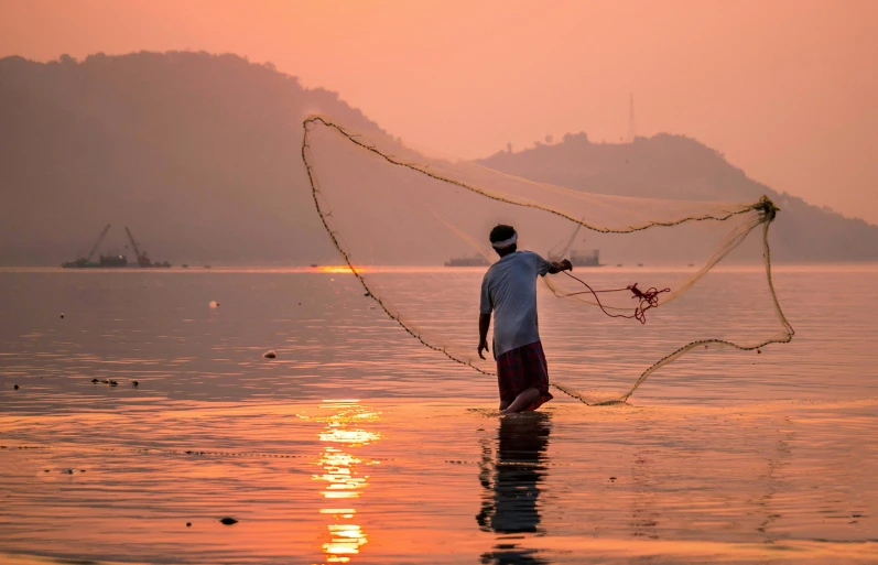 a man that is standing in the water with a net, by Rajesh Soni, pexels contest winner, warm coloured, fishing, pulling strings, early evening