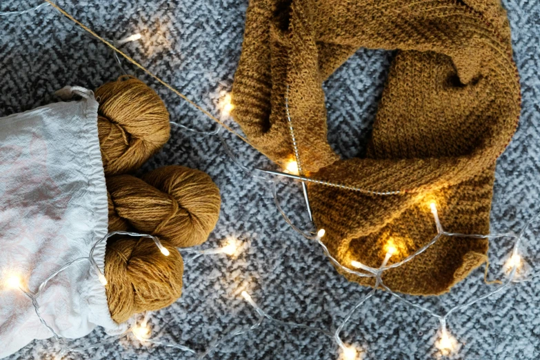 a scarf sitting on top of a blanket next to a ball of yarn, inspired by Ernest William Christmas, pexels contest winner, hurufiyya, firefly lights, brown and gold, herringbone floor, magazine photo