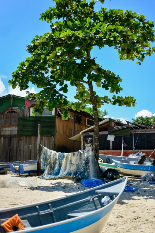 a couple of boats sitting on top of a sandy beach, by Judith Gutierrez, sumatraism, house's and shops and buildings, laundry hanging, trees outside, as photograph