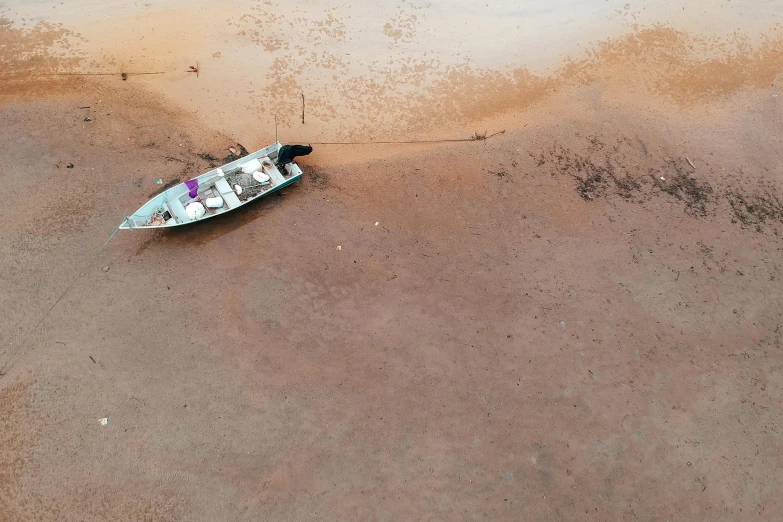 a small boat sitting on top of a sandy beach, by Peter Churcher, pexels contest winner, hurufiyya, birdseye view, dead river, shipibo, looking at the ground