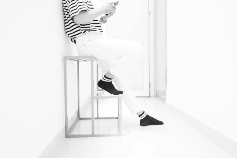 a man sitting on a stool reading a book, a black and white photo, by Emma Andijewska, unsplash, minimalism, striped socks, cai xukun, photo on iphone, white shoes