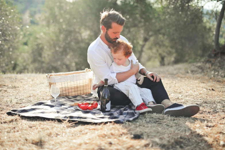 a man holding a baby while sitting on a blanket, by Julian Hatton, pexels contest winner, having a picnic, wine, 15081959 21121991 01012000 4k, white