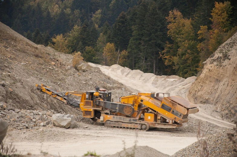 a large yellow machine sitting on top of a dirt field, unsplash, landslides, full trees, gravel and scree ground, avatar image