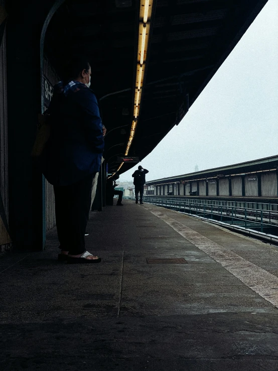 a woman waiting for a train at a train station, inspired by Louis Stettner, unsplash, hyperrealism, on liberty island, rainy; 90's photograph, two people, it's getting dark