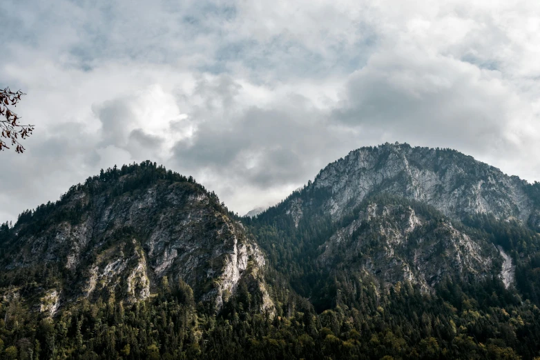 a body of water with a mountain in the background, fir trees, top selection on unsplash, gray clouds, steep cliffs