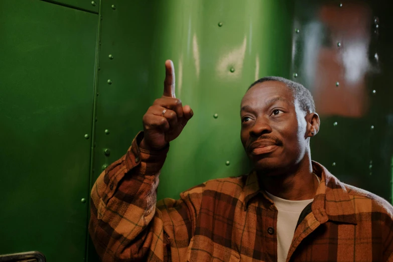 a man standing in front of a green wall, by Amos Ferguson, happening, pointing at the camera, stood in a cell, adebanji alade, aardman studios