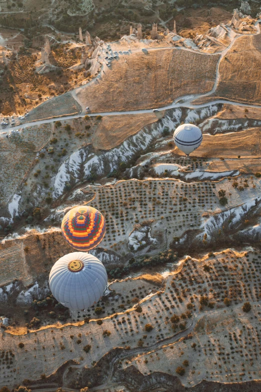 a group of hot air balloons flying over a mountain, white travertine terraces, looking down from above, warmly lit, grey