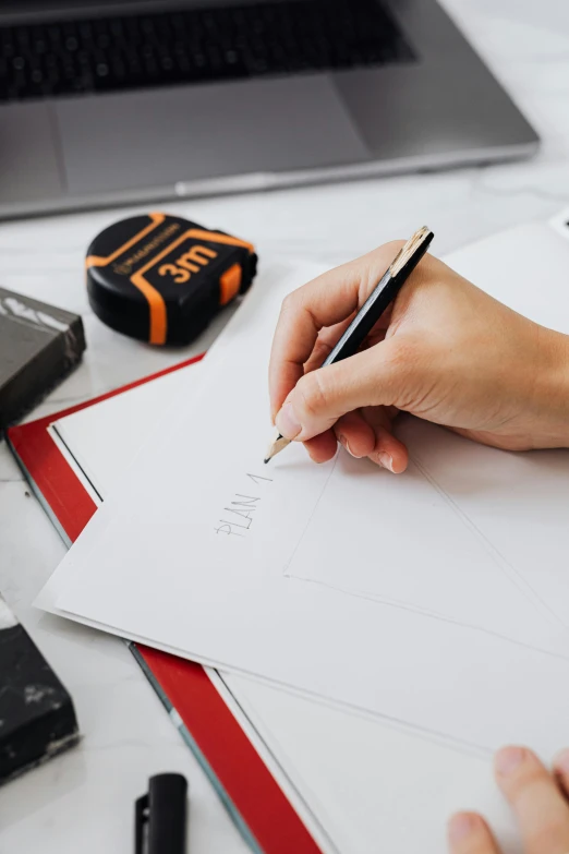 a person writing on a piece of paper next to a laptop, architectural finishes, thumbnail, educational supplies, detailed letters