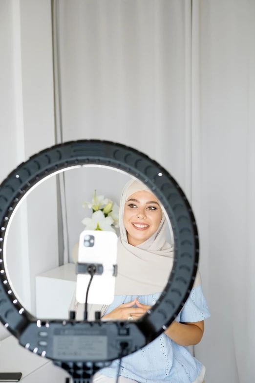 a woman standing in front of a mirror holding a camera, inspired by Nazmi Ziya Güran, hurufiyya, ring light, headset, wheel, wearing a light grey crown