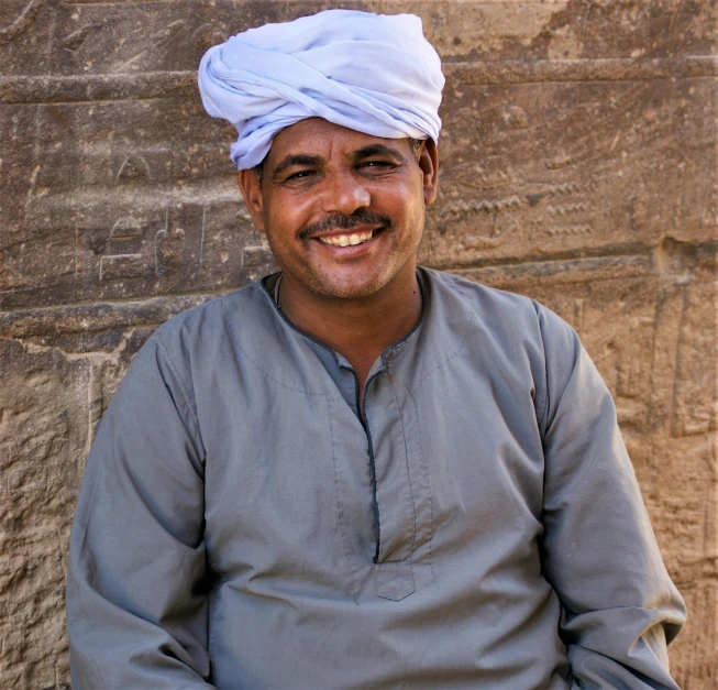 a man in a turban sitting in front of a stone wall, pexels contest winner, dau-al-set, happily smiling at the camera, from luxor, : :, engineer