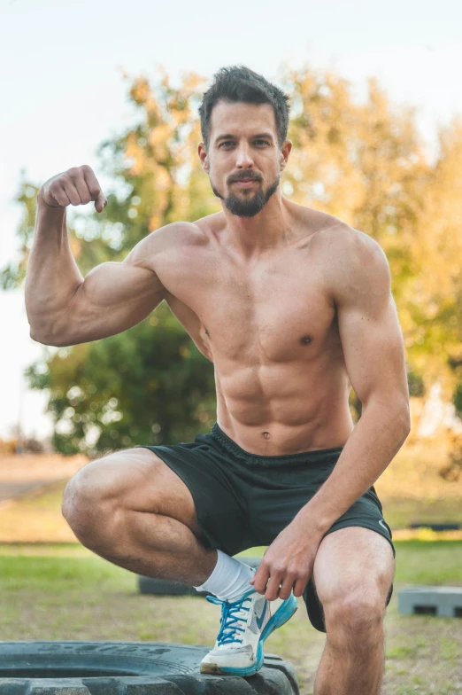 a shirtless man squatting on a tire, a stock photo, shutterstock, renaissance, at a park, showing off biceps, beto val, elongated arms