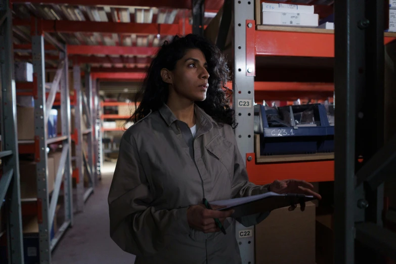 a woman standing in a warehouse holding a clipboard, pexels, arbeitsrat für kunst, young middle eastern woman, dynamic movie still, profile image, episode still