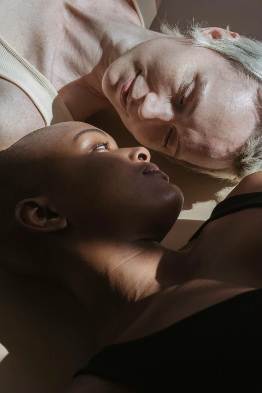 a woman laying on top of a bed next to a man, poster art, by David Donaldson, unsplash, portrait of ororo munroe, pale complexion, shaven, bathed in light