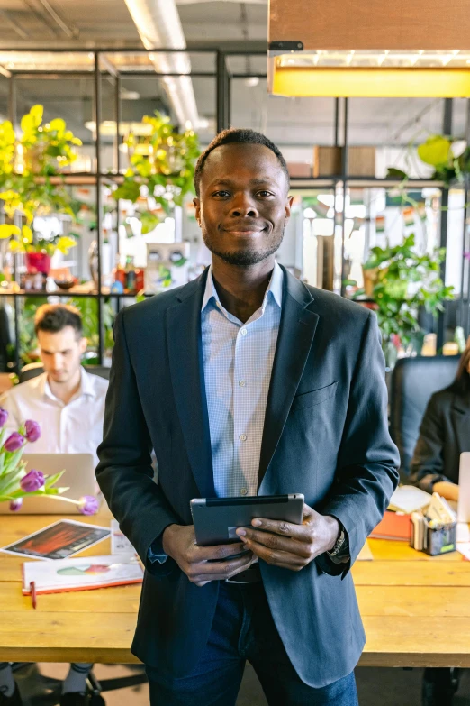 a man standing in front of a table holding a tablet, african canadian, very professional, reddit post, confident looking