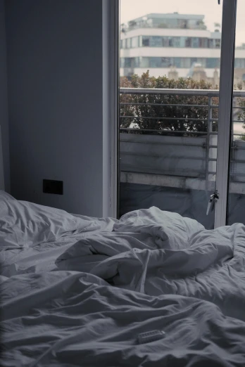 a bed sitting in a bedroom next to a window, inspired by Elsa Bleda, pexels contest winner, curled up under the covers, pathetic, ignant, dirty apartment