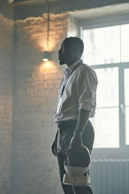 a man standing next to a window in a room, inspired by Gordon Parks, wearing a white button up shirt, **cinematic, lance reddick, back lit