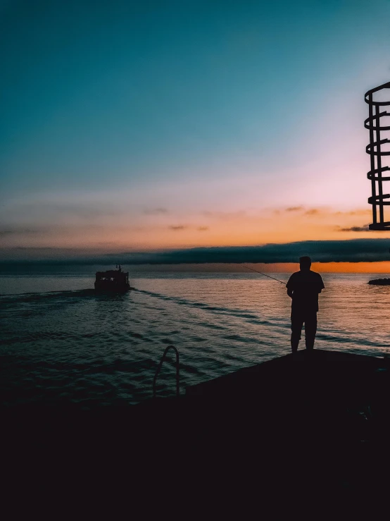 a man standing on top of a pier next to a body of water, during a sunset