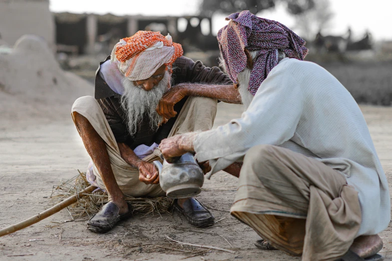 a couple of men sitting on top of a dirt field, inspired by Steve McCurry, pexels contest winner, peacefully drinking river water, turban, old man doing hard work, lachlan bailey
