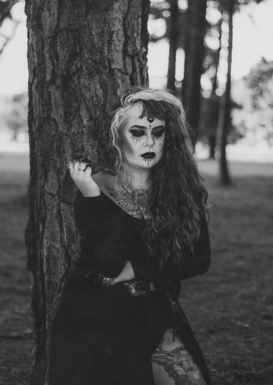 a woman with makeup standing next to a tree, a black and white photo, tumblr, gothic art, portrait featured on unsplash, witchcore, portrait of a zombie, ✨🕌🌙