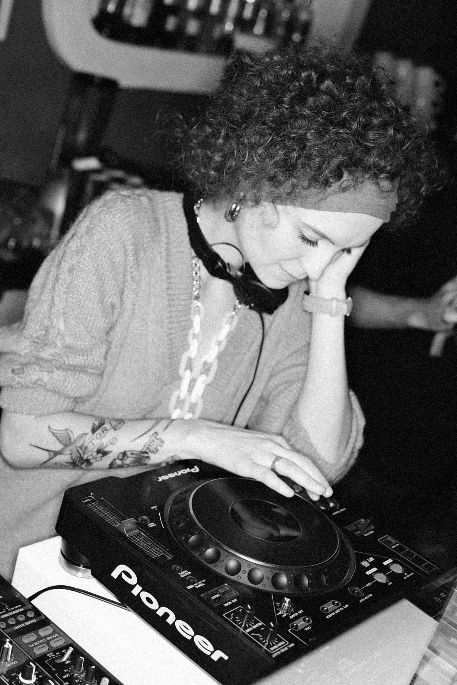 a black and white photo of a woman playing a dj, with a curly perm, turntablism dj scratching, vivienne westwood, taken in the late 2010s