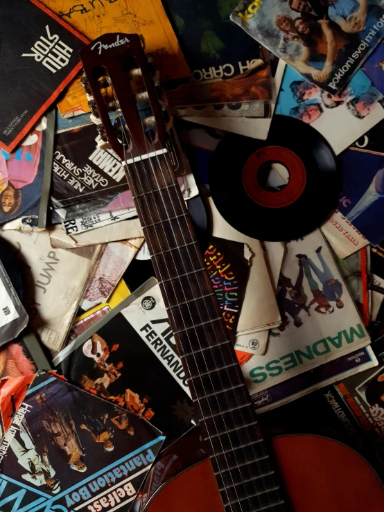 a guitar sitting on top of a pile of cd's, an album cover, inspired by William Harnett, trending on pexels, ( ( theatrical ) ), magazine scraps, looking across the shoulder, vhs artefacts