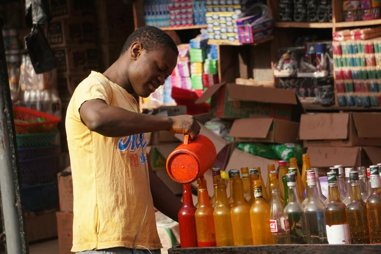 a man standing in front of a cart filled with bottles, by Ingrida Kadaka, pexels, happening, a brightly colored, holding a drink, orisha, working