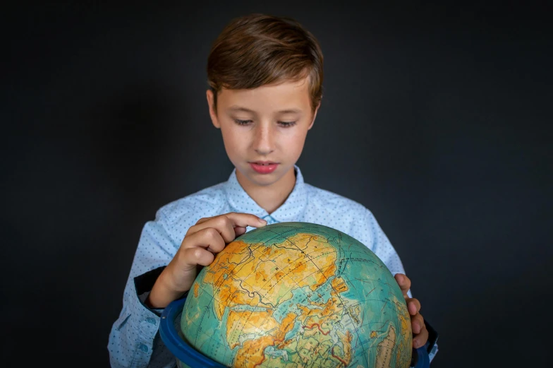 a young boy holding a globe in his hands, an album cover, by Adam Marczyński, pexels contest winner, well-groomed model, school class, holding an epée, product introduction photo