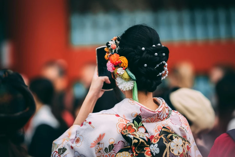 a woman holding a cell phone up to her ear, a picture, inspired by Uemura Shōen, trending on unsplash, elaborate costume, hair styled in a bun, back to camera, floral clothes