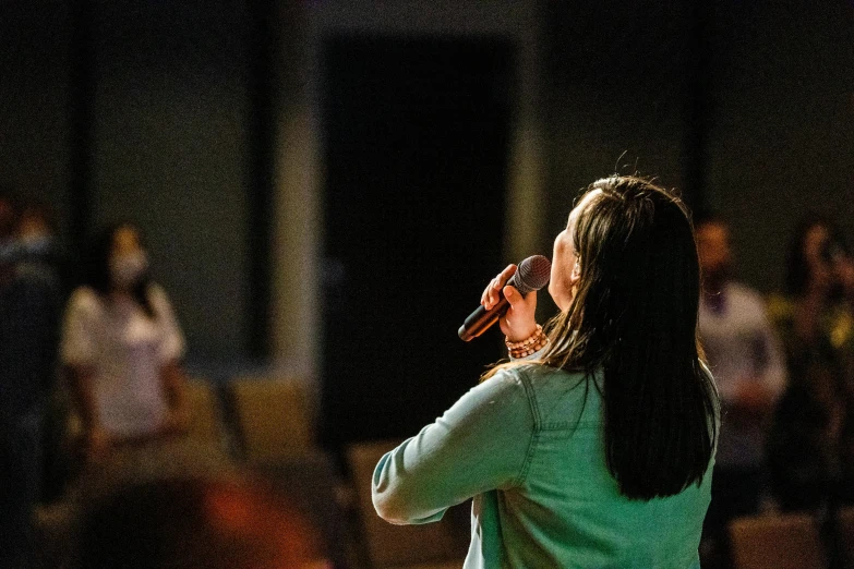 a woman standing in front of a crowd talking on a cell phone, tabernacle deep focus, promo image, holding microphone, college