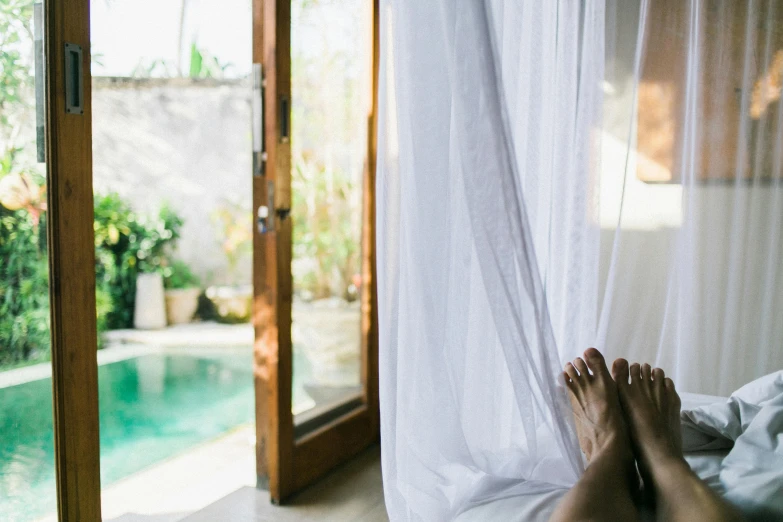 a person laying on a bed next to a pool, light and space, ethereal curtain, unsplash photography, french door window, paradise garden massage