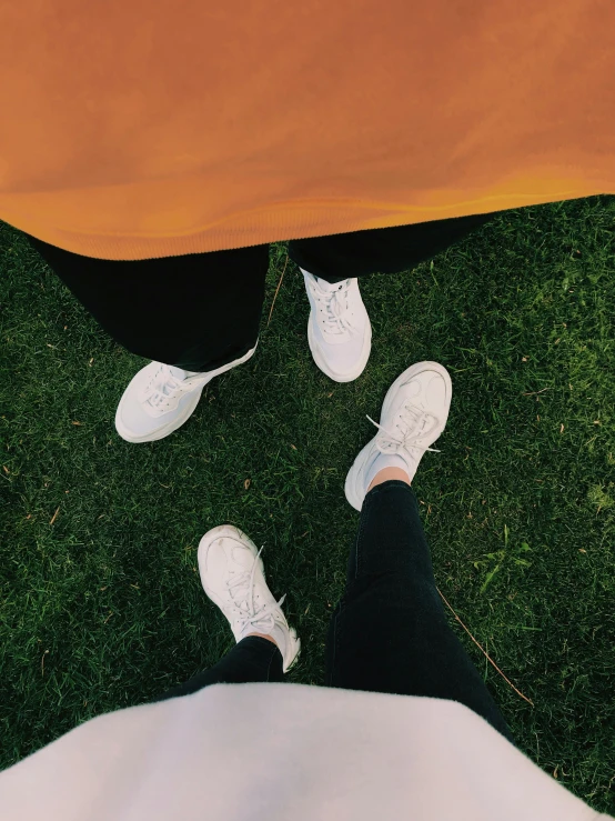 a couple of people standing on top of a lush green field, a picture, happening, wearing white sneakers, ✨🕌🌙, trending on vsco, white and orange