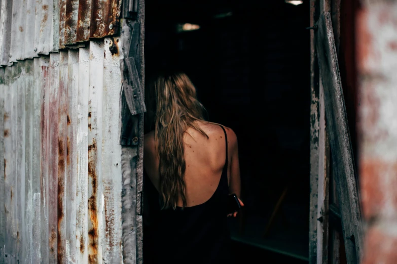 a woman standing in the doorway of a building, inspired by Elsa Bleda, pexels contest winner, happening, bare back, dirty blonde hair, shack close up, alana fletcher