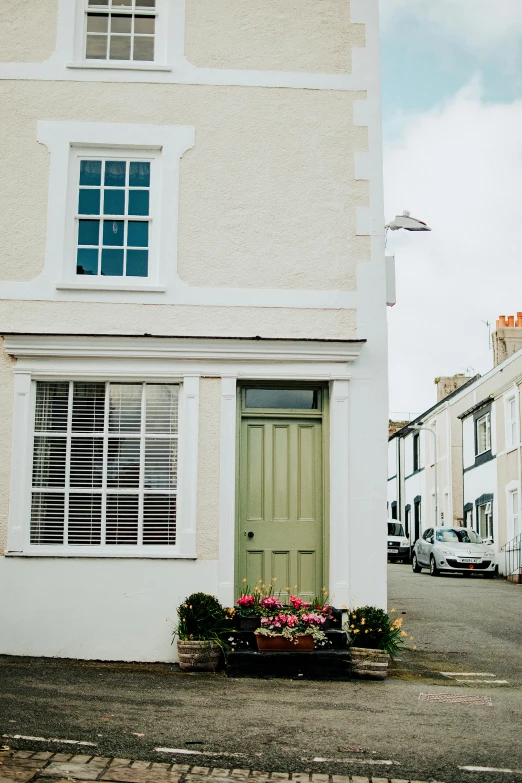 a white building with a green door and windows, unsplash, arts and crafts movement, seaview, busy small town street, 4 k image, flowery cottage