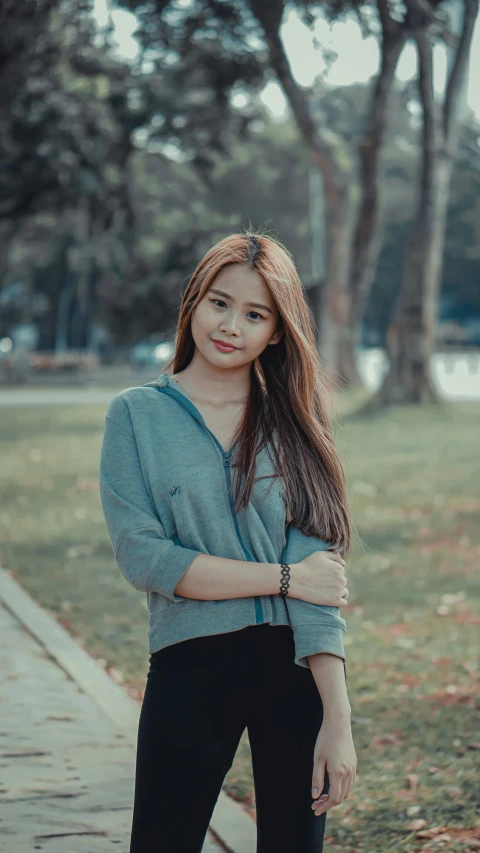 a woman standing on a sidewalk in a park, a colorized photo, inspired by Natasha Tan, pexels contest winner, realism, young cute wan asian face, grey hoodie, gif, young with long hair